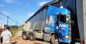 Carreta bate em caminhão, sai da pista e atinge parede de empresa