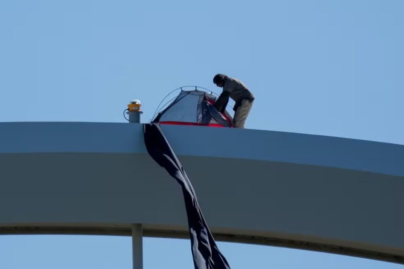 Manifestante escala ponte para protestar contra Trump, guerra no Irã e IA